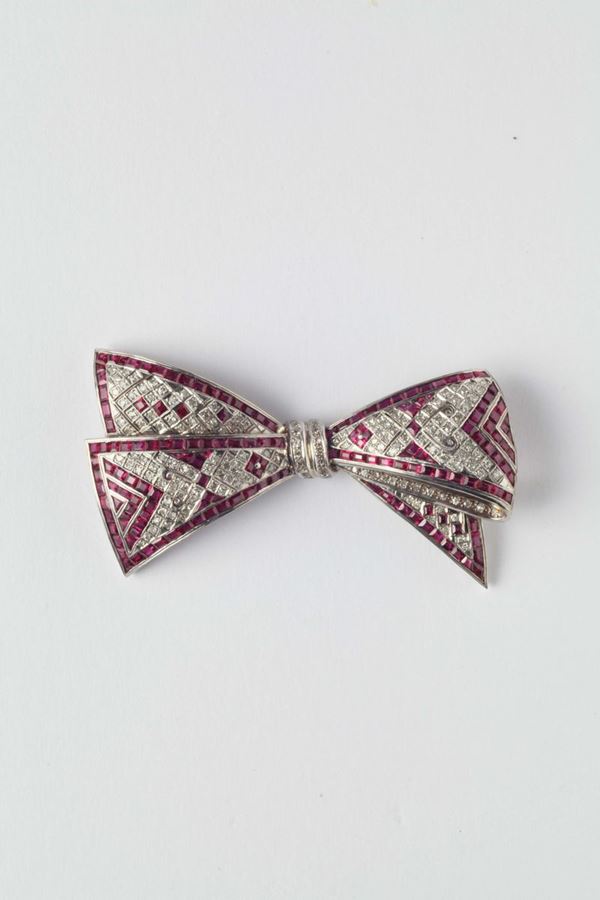 A diamond and ruby ribbon bow brooch. 1950s