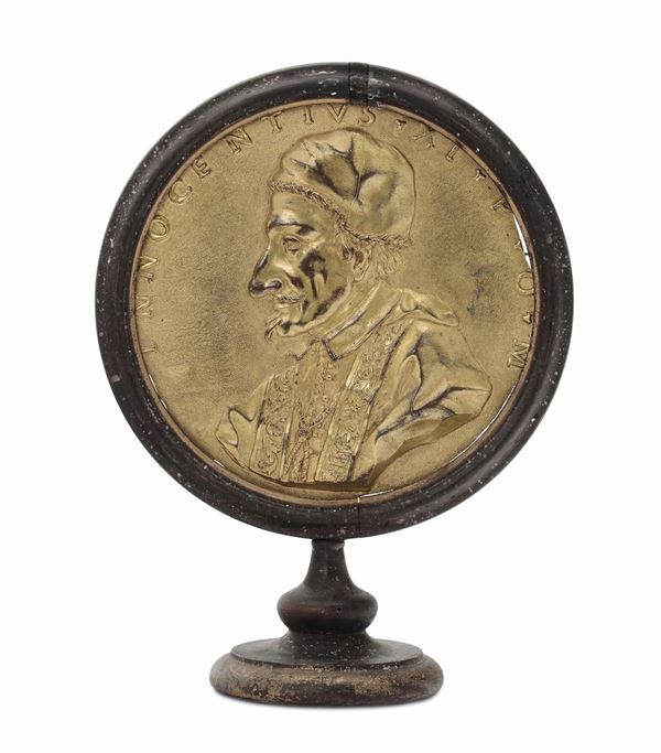 A circular molten, chiselled and gilt bronze plate representing the profile of Pope Clement 11th, Rome 18th century, ebonised wood frame with circular foot