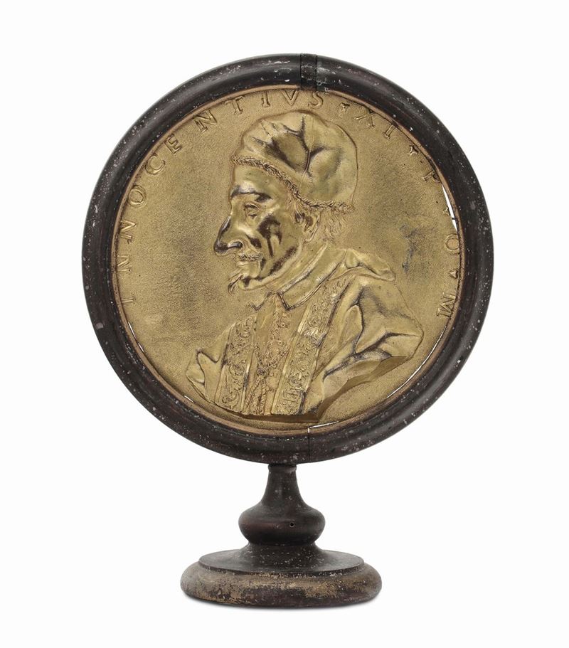 A circular molten, chiselled and gilt bronze plate representing the profile of Pope Clement 11th, Rome 18th century, ebonised wood frame with circular foot  - Auction Sculpture and Works of Art - Cambi Casa d'Aste