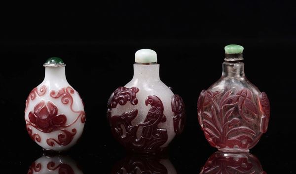 Three glass snuff bottles with red vegetable decoration in relief, one with a lotus flower, one with a parrot and one with water lilies, China, 20th century