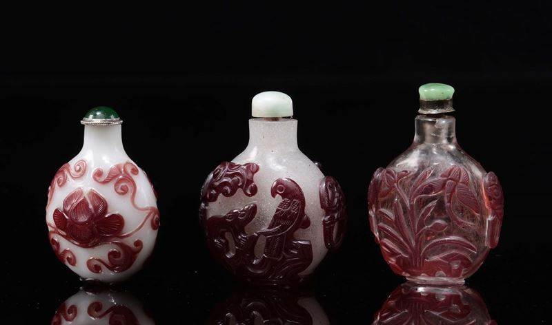 Three glass snuff bottles with red vegetable decoration in relief, one with a lotus flower, one with a parrot and one with water lilies, China, 20th century  - Auction Chinese Works of Art - Cambi Casa d'Aste