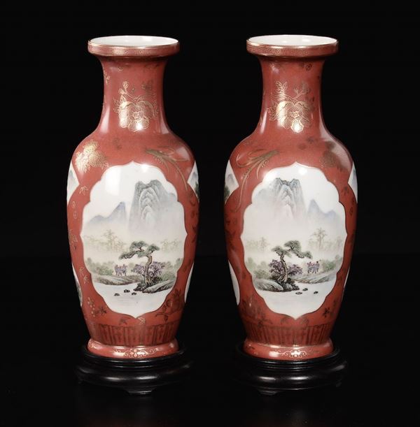 Coppia di vasi in porcellana a fondo rosso con smalti policromi con paesaggio fluviale e alberi entro riserve, Cina, XX secolo