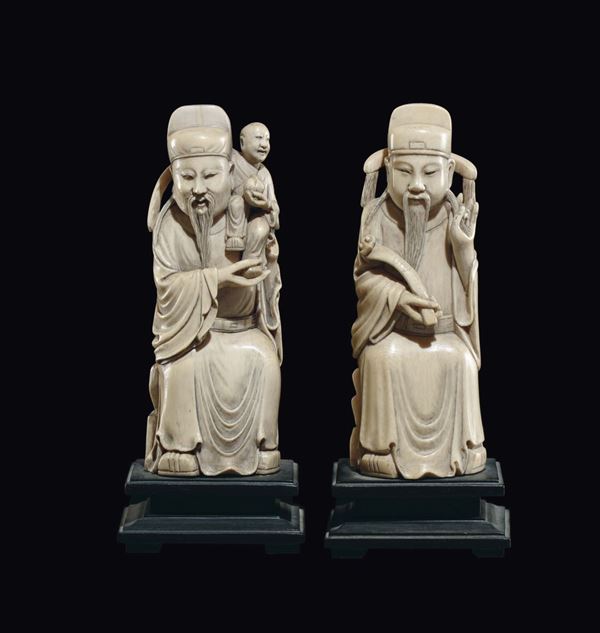 A pair of carved ivory sitting dignitaries, one with a ruyi and one with child on his shoulder, China, early 20th century