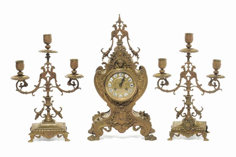 Trittico Napoleone III in ottone patinato composto da orologio e due candelabri a tre luci, Francia fine XIX secolo  - Asta Arredi dalle dimore degli eredi Ercole Marelli e altre provenienze - Cambi Casa d'Aste
