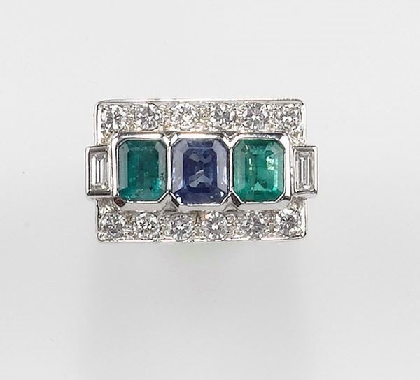 An emerald, sapphire and diamond ring. The two emeralds, sapphires and pavé set diamonds are mounted in white gold 750/1000