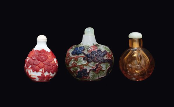 Lotto di tre snuff bottles in vetro e pasta di vetro con decoro a rilievo, una con tartaruga, una con fiore di loto e pagoda rossa ed una con alberi, Cina, inizio XX secolo