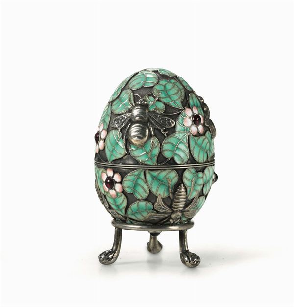 An egg in gilt silver, cloisonné enamels and cabochon garnets with a tripodal pedestal. Russian manufacture, Moscow, punches in use from 1908 to 1917