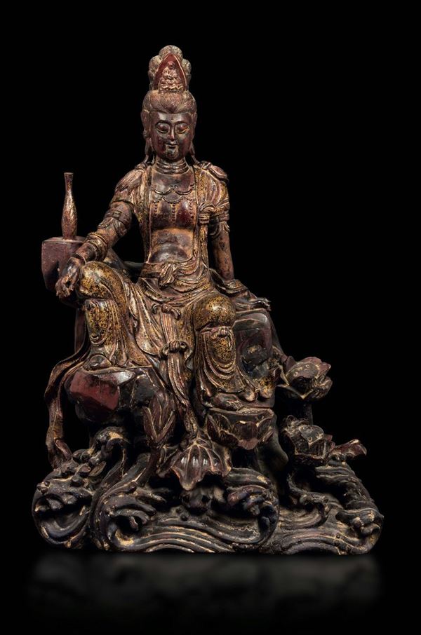 A partially lacquered wooden sculpture depicting Guanyin seated on a rock with gold floral decors, China, Ming Dynasty, early 17th century