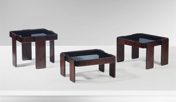Set di tre tavoli bassi impilabili con struttura in legno e piano in vetro.