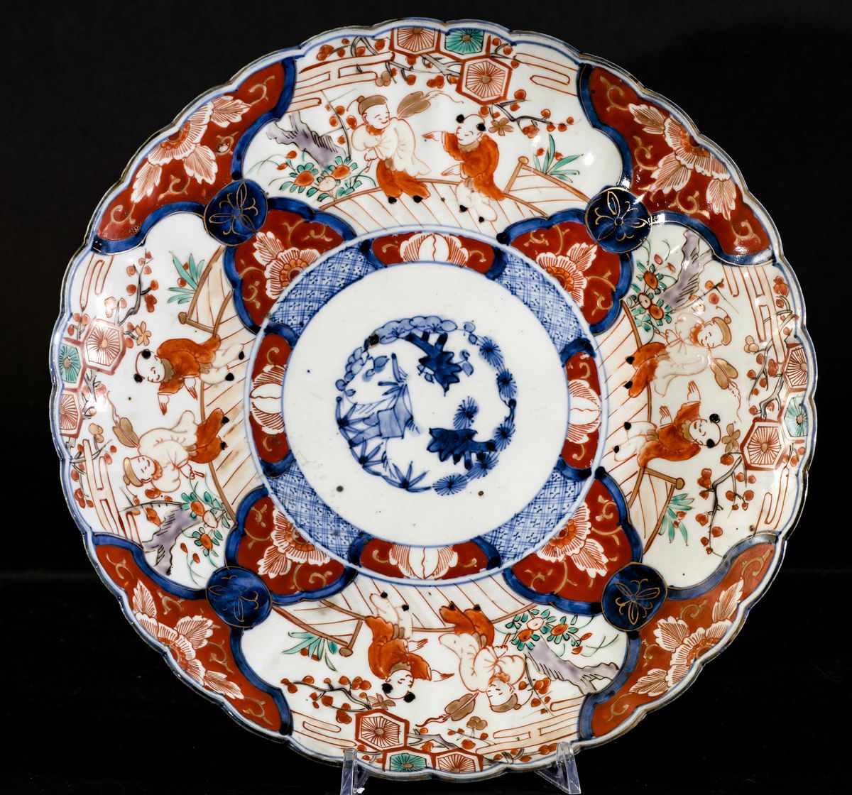 Piatto in Porcellana Imari con Decori Naturalistici e Scene di Vita Comune Entro Riserve, Giappon...