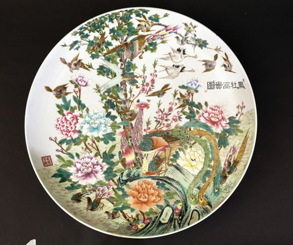 Grande piatto in porcellana a smalti policromi raffigurante scena naturalistica con pavoni, peonie in fiore e iscrizione, Cina, Repubblica, XX secolo