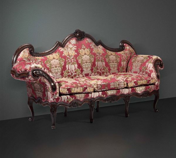 Due divani a orecchioni in noce riccamente intagliati e tessuto rosso con decori floreali, Lombardia XVIII secolo