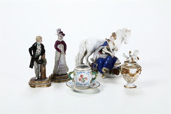Lotto di cinque porcellane diverse tra cui un gruppo equestre, due figurine di damerini, un vasetto con coperchio e una mostardiera con piattino. XIX e XX secolo.