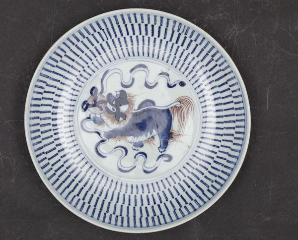 Piatto in porcellana con figura di cane di Pho nei toni del blu e del rosso ferro, Cina, Dinastia Qing, XIX secolo