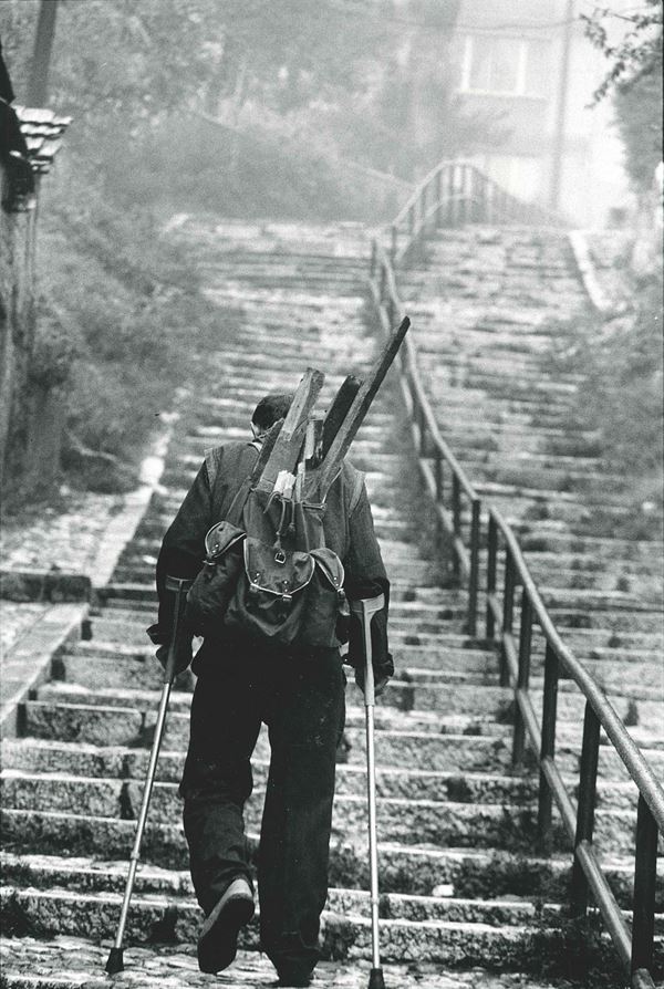 A man on crutches carries wood for fuel in his rucksack. Bosnie-Herzigovine, Sarajevo