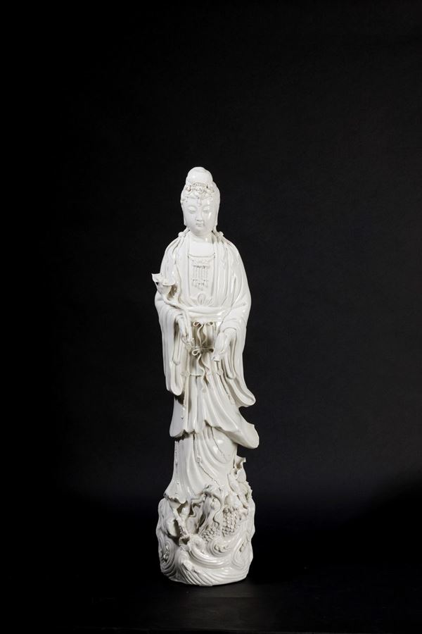 Figura in porcellana Blanc de Chine raffigurante Guanyin eretta su con vasetto, ramo fiorito e drago sulla base, Cina, inizi XX secolo