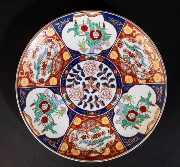 Piatto in porcellana Imari con decori floreali e soggetti naturalistici entro riserve, Giappone, XX secolo