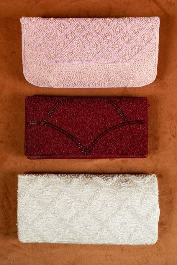 Portafoglio Loewe in seta bianca ricamato a motivi di ghirlande con fiori e perline, portafoglio di seta rossa ricoperto di perline e portafoglio in seta rosa ricoperto di perline rosa e perle.