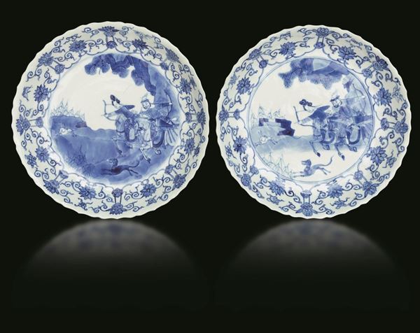 Coppia di piatti in porcellana bianca e blu con scene di caccia e decori floreali, Cina, Dinastia Qing, epoca Kangxi (1662-1722)