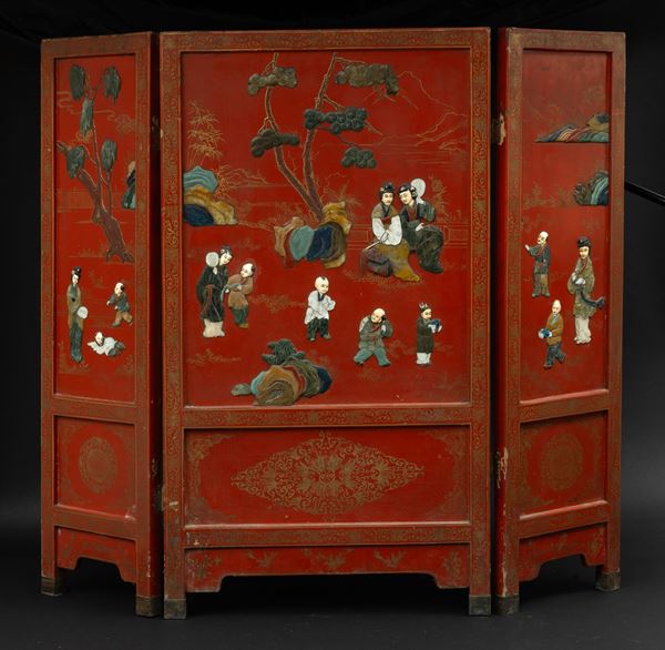 Paravento a tre ante in legno rosso laccato e applicazioni in pietre dure raffigurante scene di vita comune a rilievo, Cina, XIX secolo