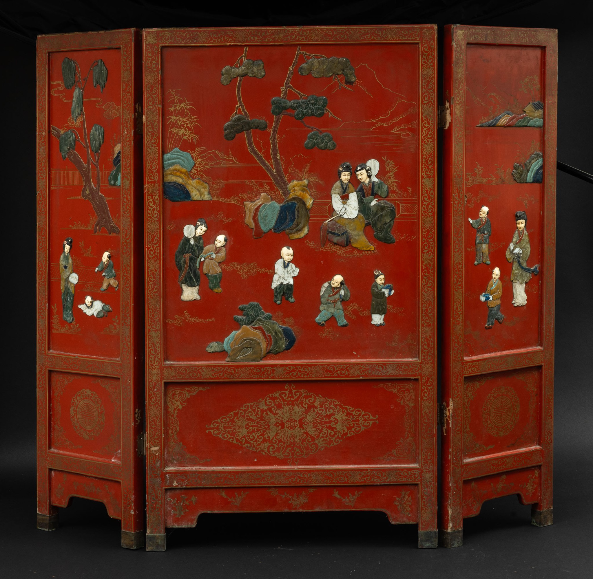 Paravento a tre ante in legno rosso laccato e applicazioni in pietre dure raffigurante scene di v...