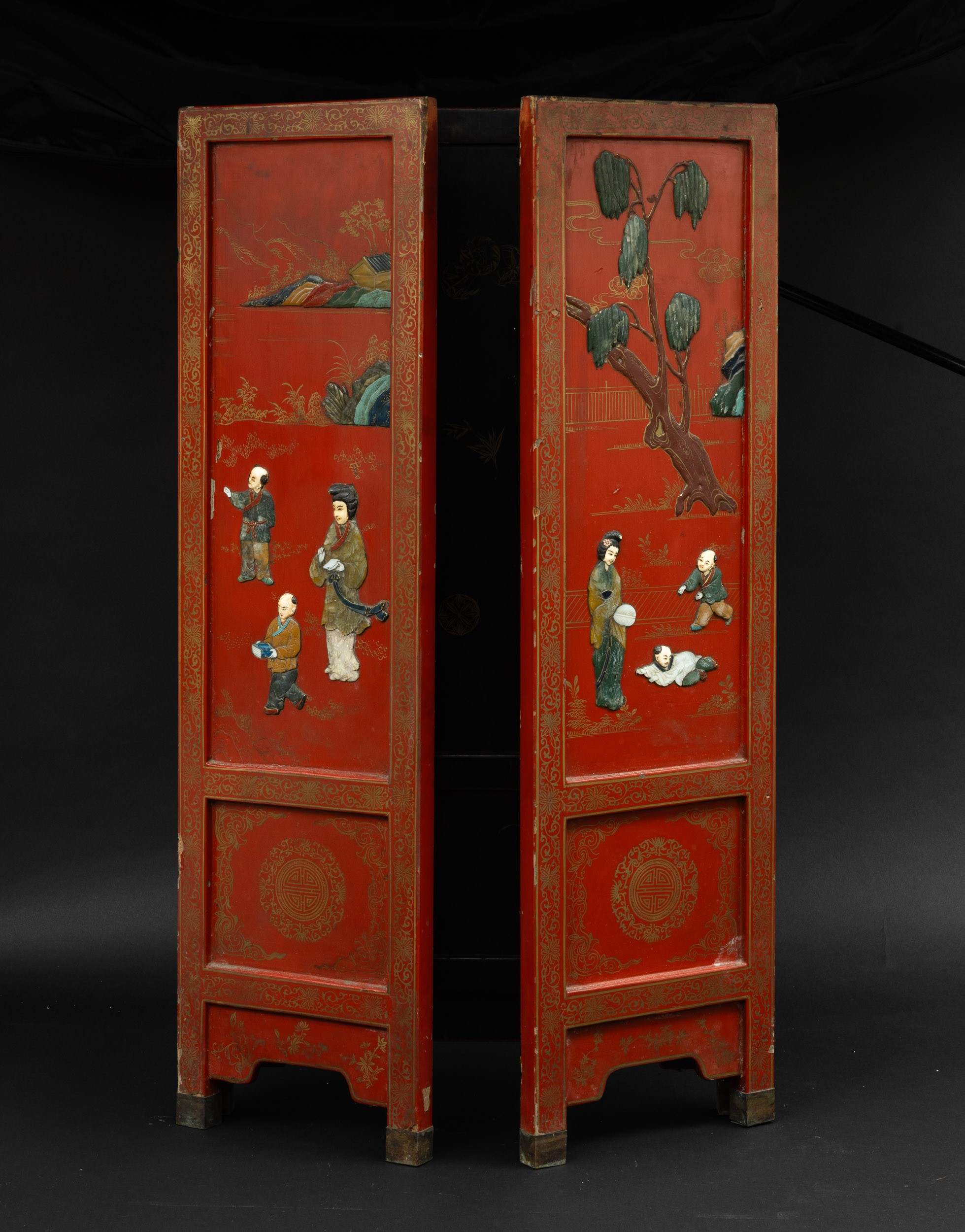Paravento a tre ante in legno rosso laccato e applicazioni in pietre dure raffigurante scene di v...