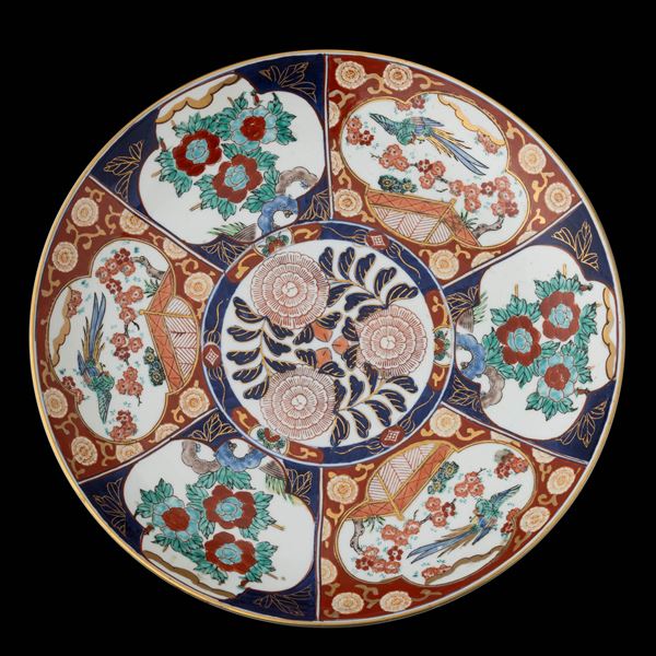 Piatto in porcellana Imari con decori floreali e soggetti naturalistici entro riserve, Giappone, XX secolo