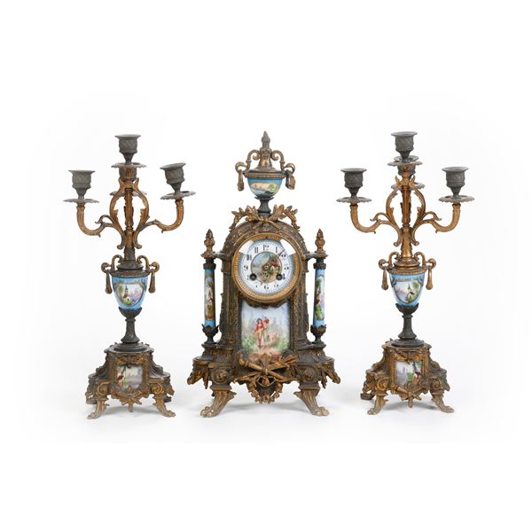 Trittico da camino in bronzo e porcellana dipinta composto da orologio e coppia di candelabri. Francia XIX secolo