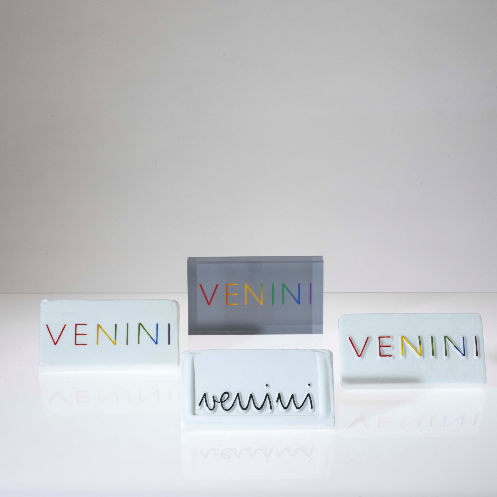 Venini, Lotto di quattro placche pubblicitarie in vetro lattimo e plexiglass, cm 16x9