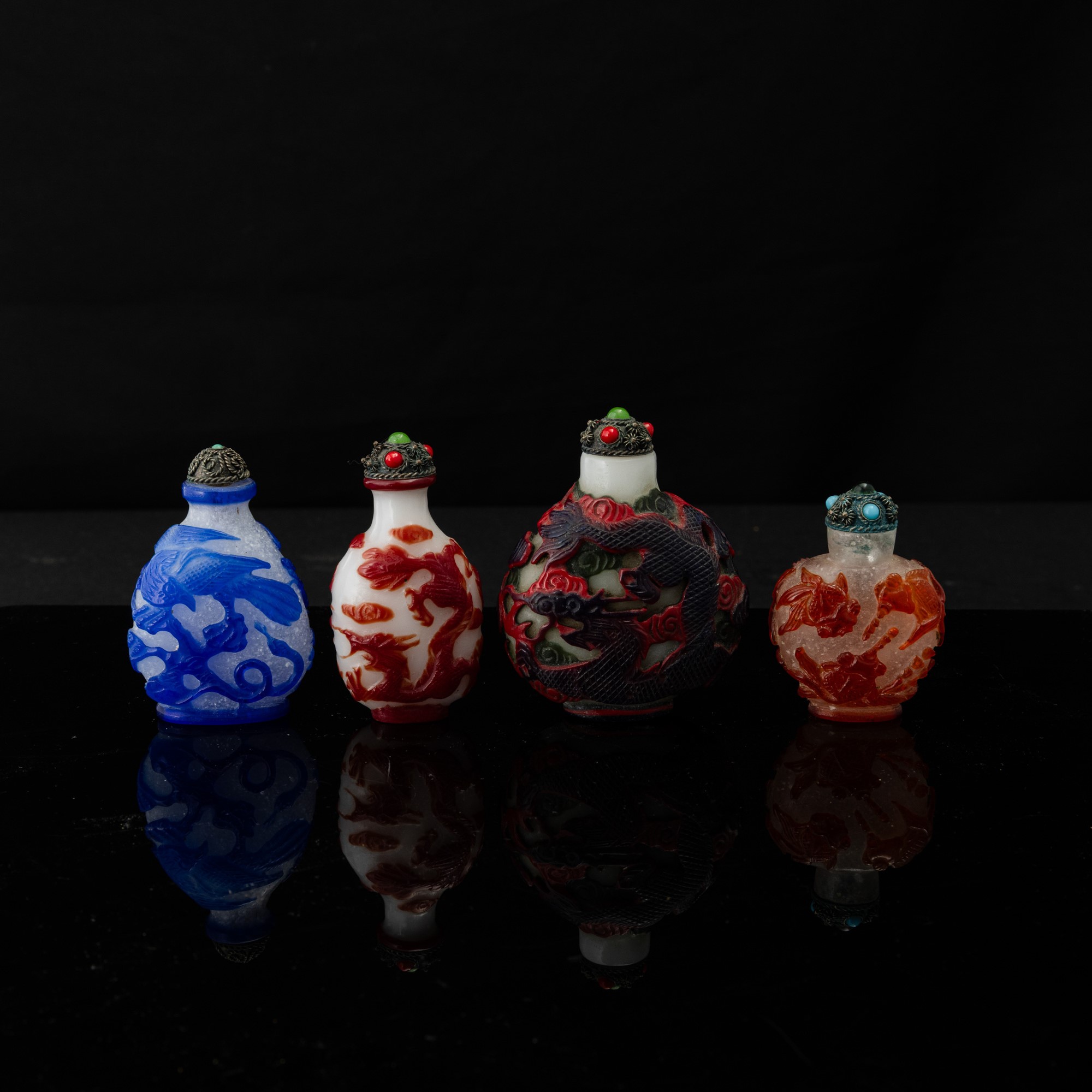 Cina, Quattro snuff bottle in vetro di Pechino con decorazione a rilievo di draghi e inserti di p...