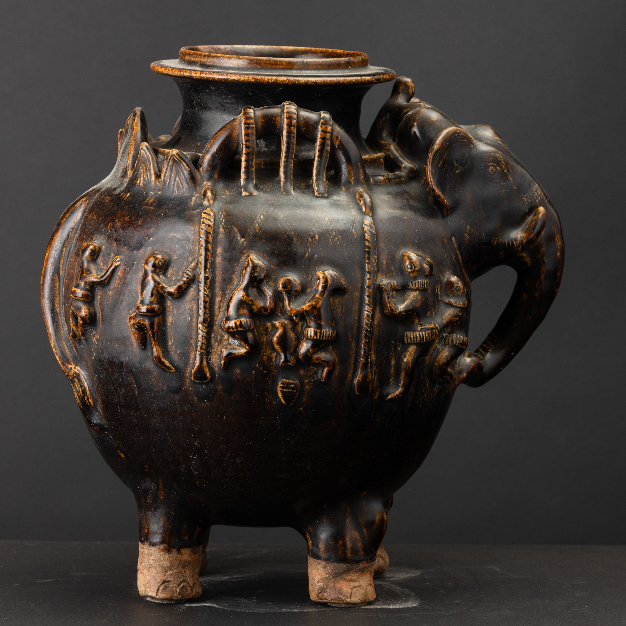 Arte Khmer, Vaso in terracotta invetriata a fondo marrone con testa di elefante e figure a riliev...