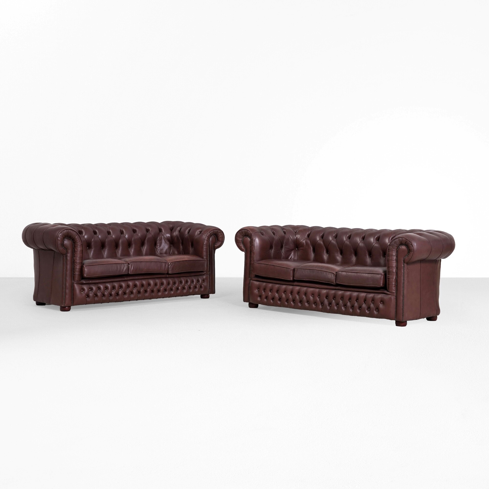 Coppia di divani modello “Chesterfield”, rivestiti in pelle, schienale capitonné (XX secolo)